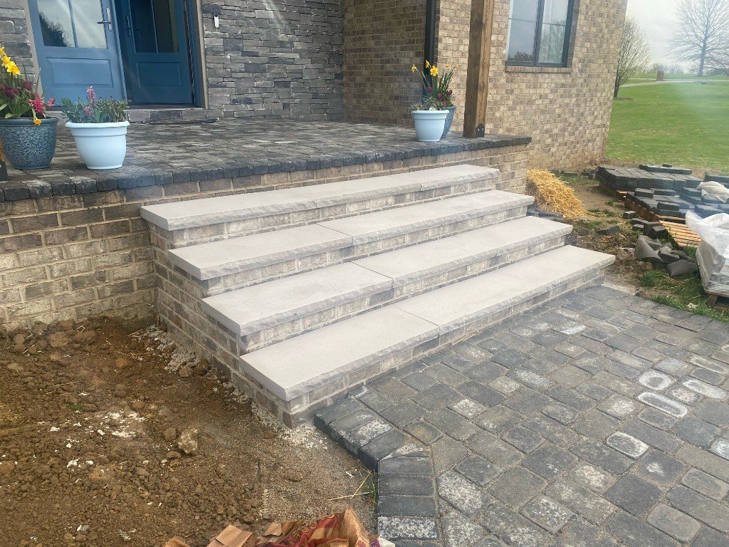 Finished stone steps and paver patio at a brick home entrance